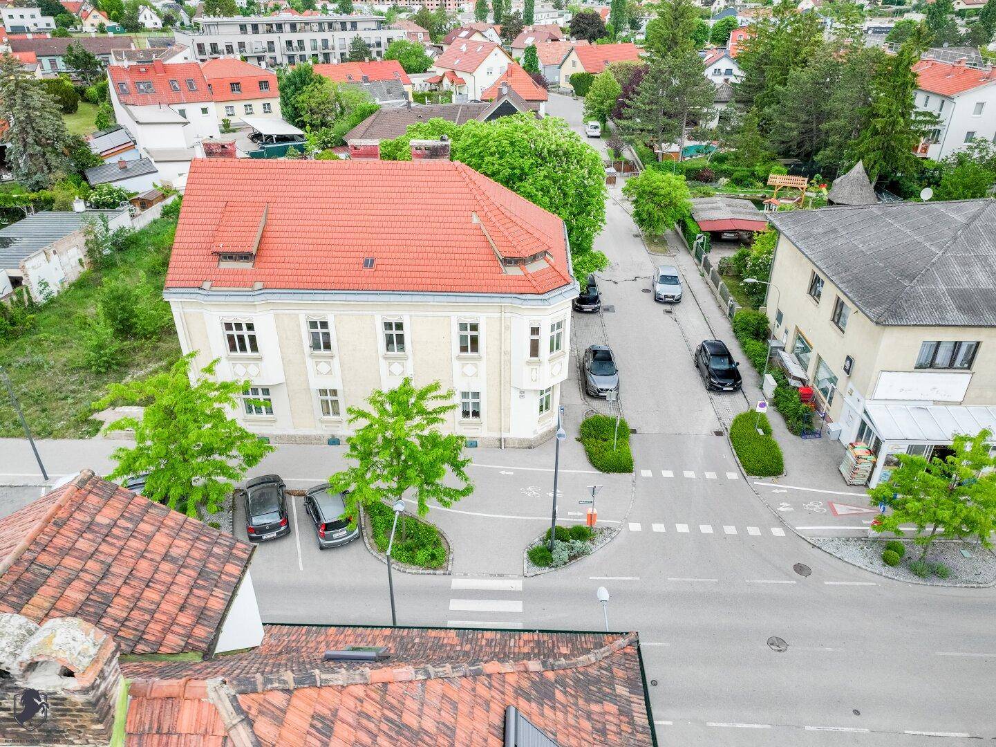 Vogelperspektive auf das historische Gebäude und die umliegende Wohngegend mit viel Grün.