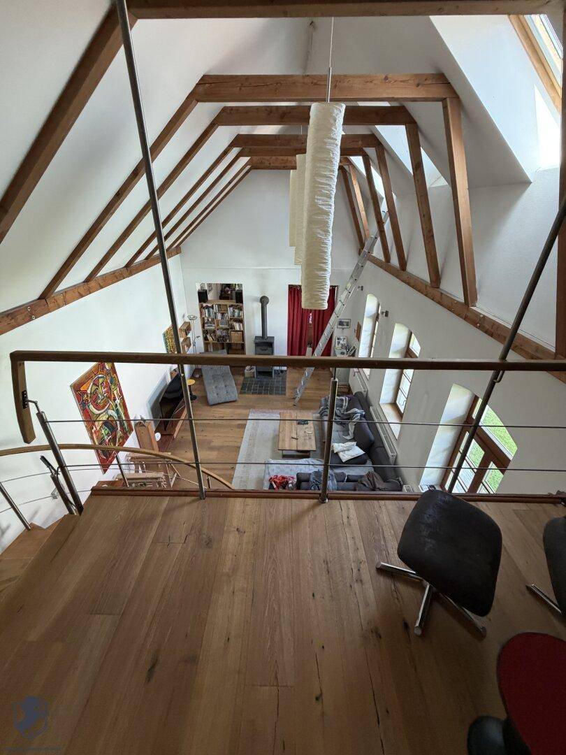 Blick von der Galerie in das offene Wohnzimmer mit hohen Decken, sichtbaren Holzbalken und viel Licht.