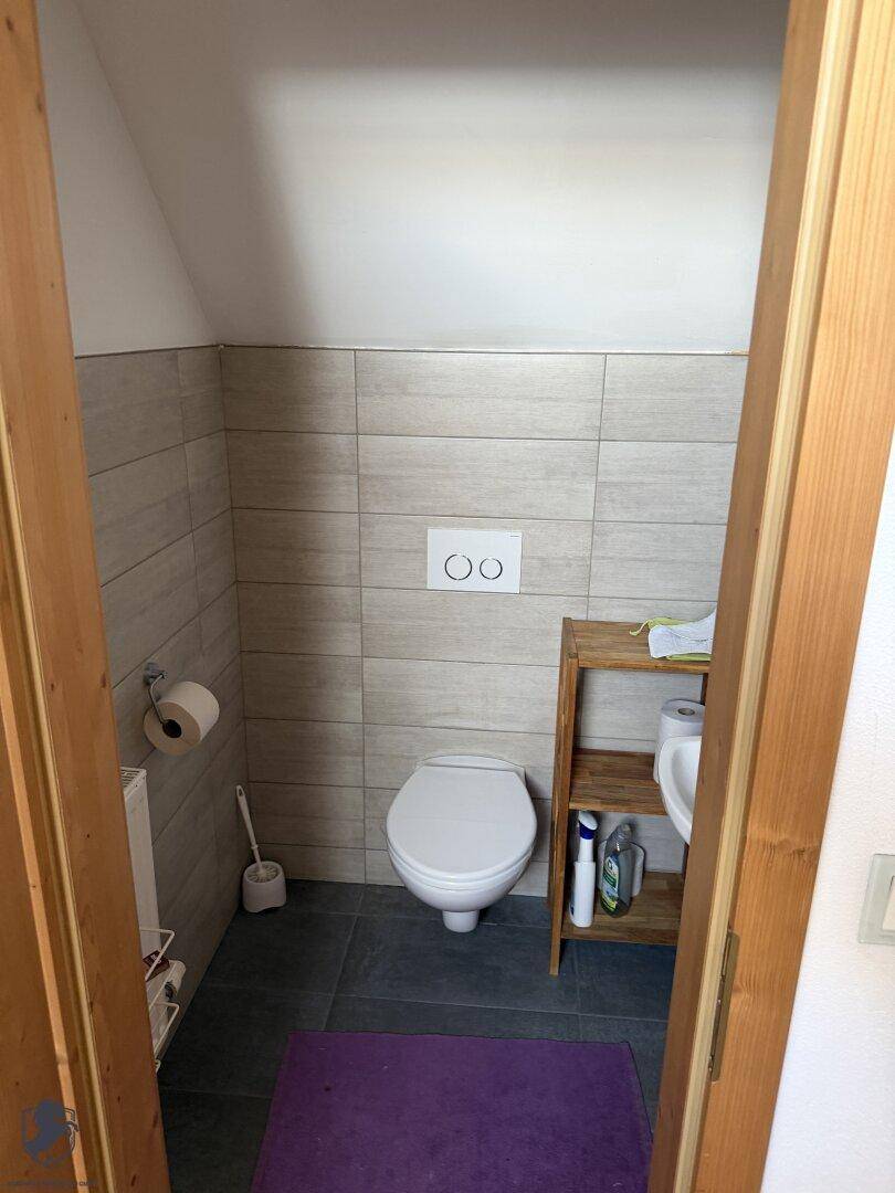 Kleines Gäste-WC mit Toilette, Waschbecken und hellen Fliesen unter einer Dachschräge.