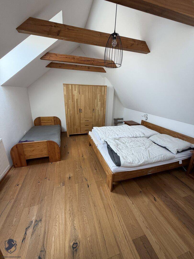 Schlafzimmer mit zwei Holzbetten, Holzschrank, Holzboden und sichtbaren Holzbalken unter Dachschräge.