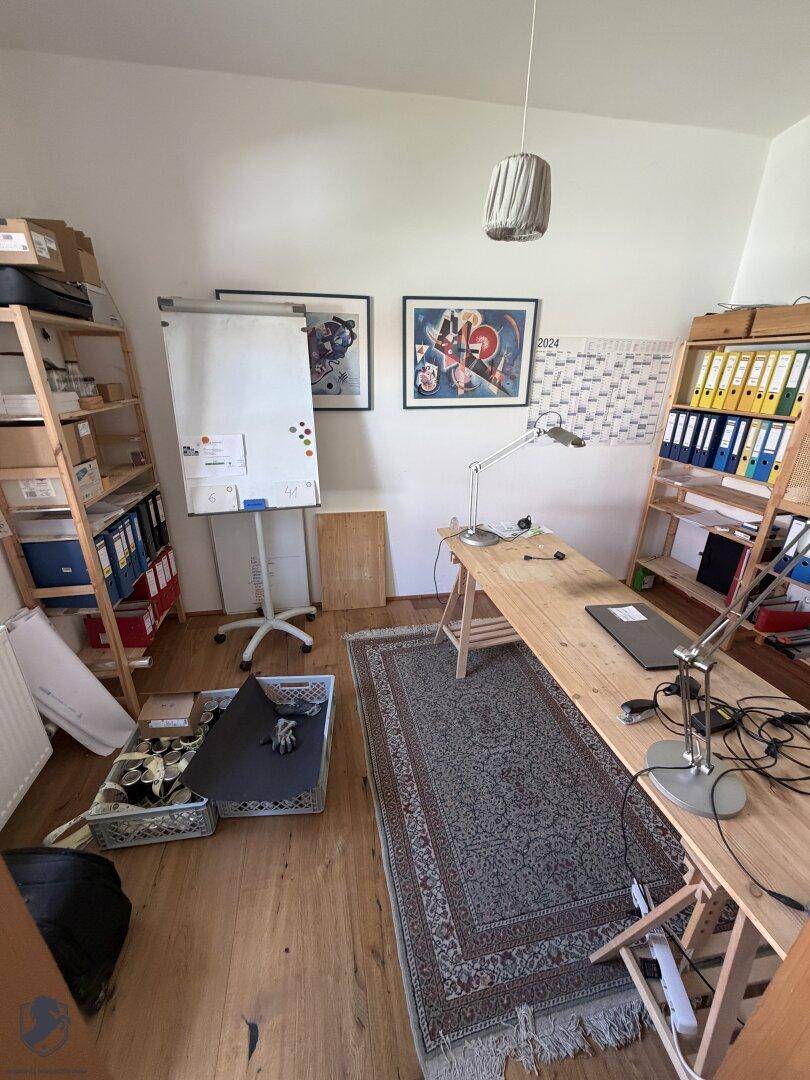 Arbeitszimmer mit Holzboden, Schreibtisch, Regalen und einem Whiteboard, hell und funktional eingerichtet.