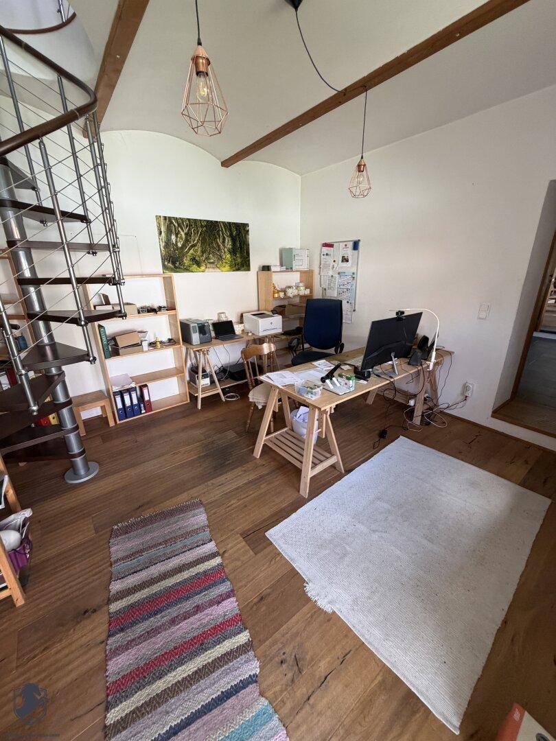 Geräumiges Arbeitszimmer mit Holzboden, Schreibtisch, Regalen und einer Wendeltreppe, sichtbare Holzbalken.