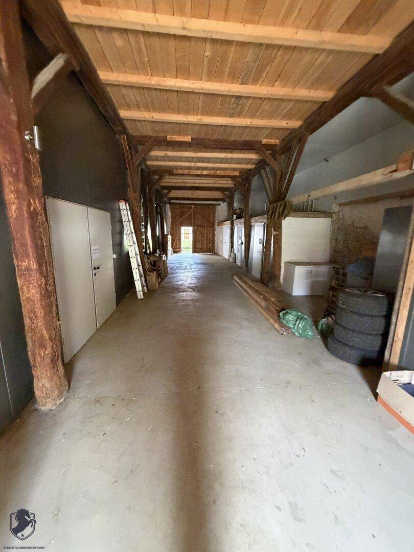 Langer, leerer Scheunenraum mit Betonboden und sichtbaren Holzbalken, ideal für Lagerung oder Umbau.