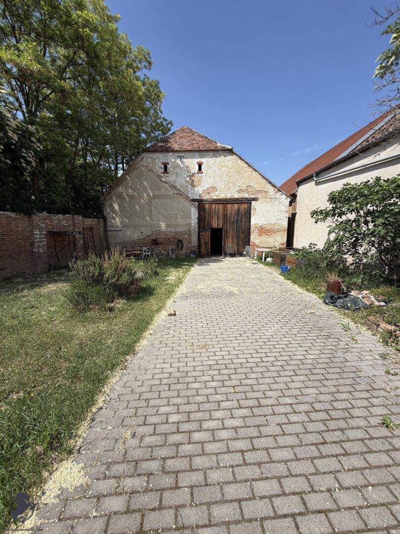 Außenansicht einer alten Scheune mit großem Holztor, gepflasterter Zufahrt und umgebendem Grün.