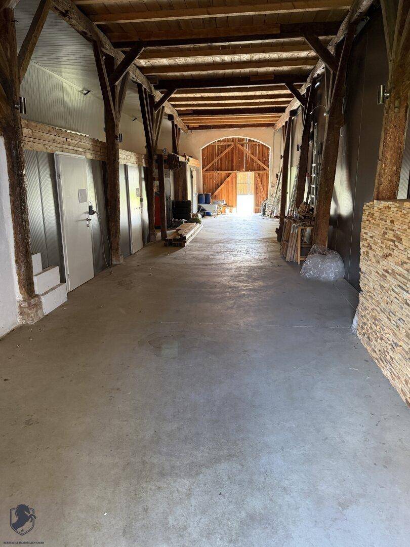Geräumiger Innenbereich mit sichtbaren Holzbalken und Betonboden, der auf eine Scheune oder Lagerhalle hindeutet.