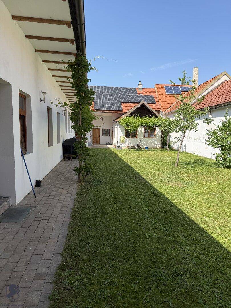 Grüner Gartenbereich mit Rasenfläche und einem Gebäude im Hintergrund, das Solarpaneele auf dem Dach hat.
