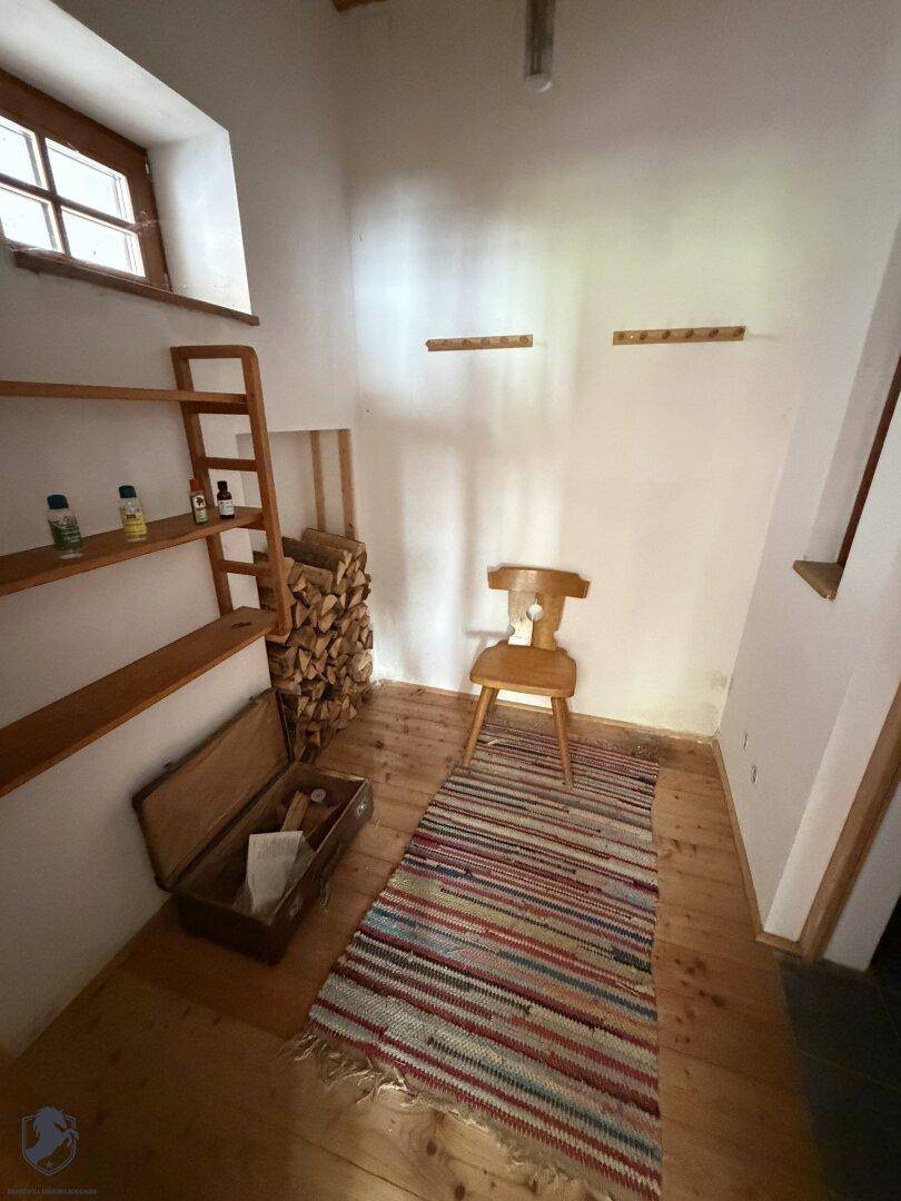 Kleiner Raum mit Holzregalen, einem Teppich und gestapeltem Brennholz, möglicherweise ein Abstellraum.