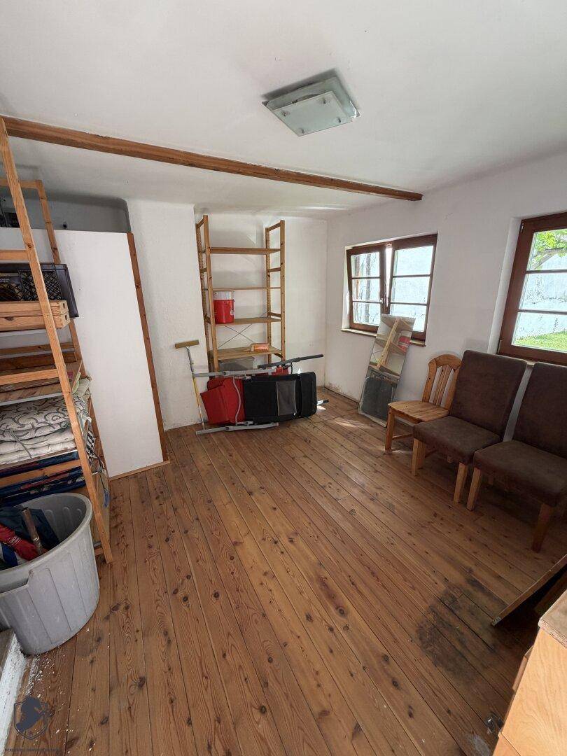 Heller Raum mit Holzdielenboden und Fenstern, der als Abstellraum oder zukünftiges Zimmer genutzt werden könnte.