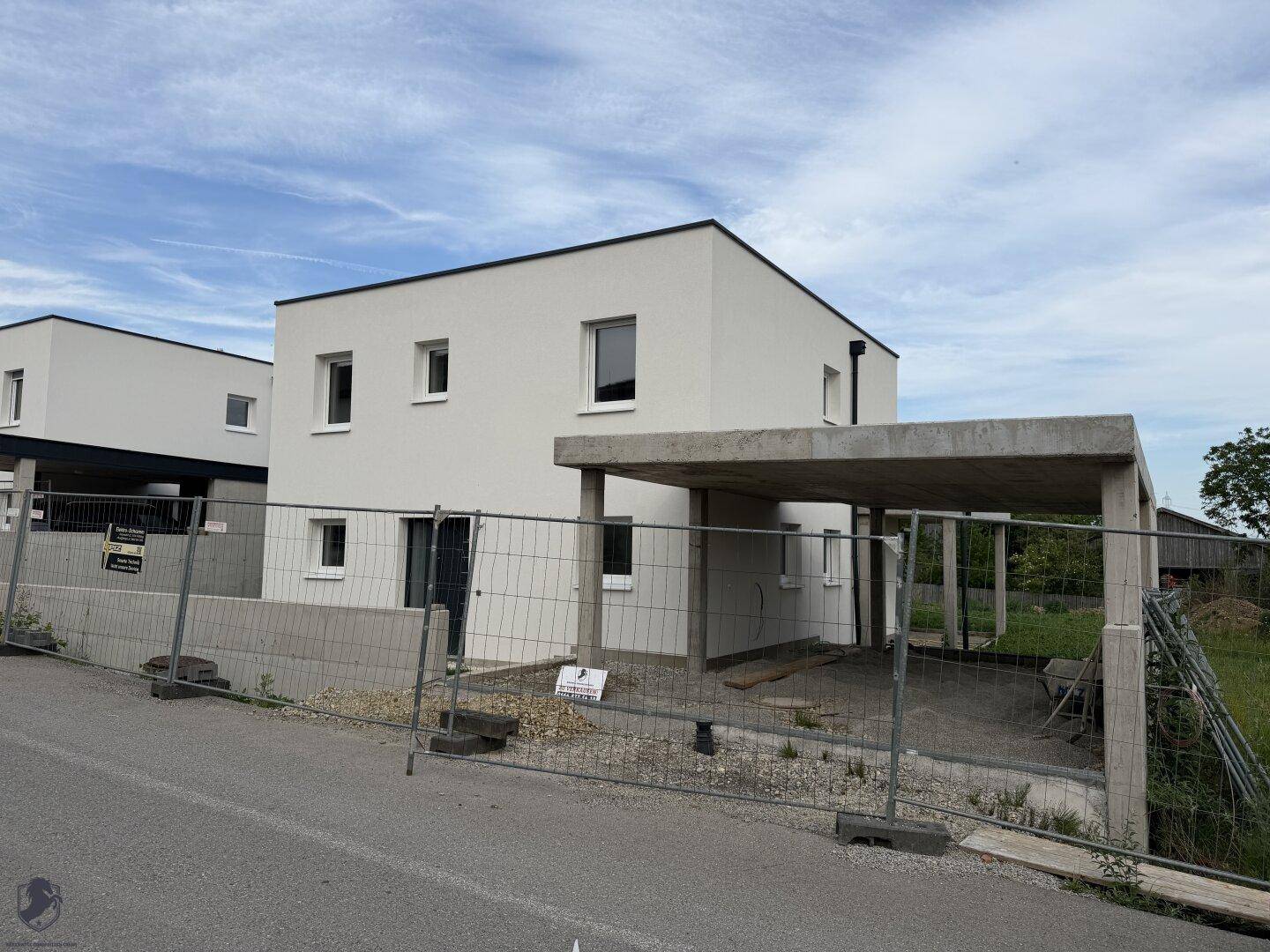 Neubau-Einfamilienhaus mit weißer Fassade und Carport-Vorbereitung an der Straße.