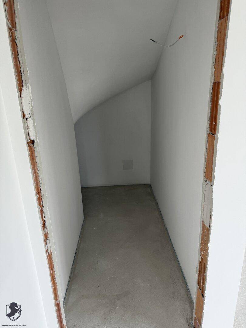 Kleiner Abstellraum unter der Treppe mit schrägen Wänden und Rohbetonboden.