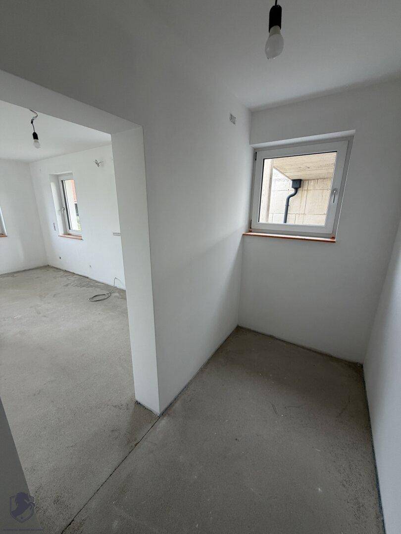 Kleiner Raum im Rohbau mit Fenster und Rohbetonboden, ideal als Büro oder Gästezimmer.