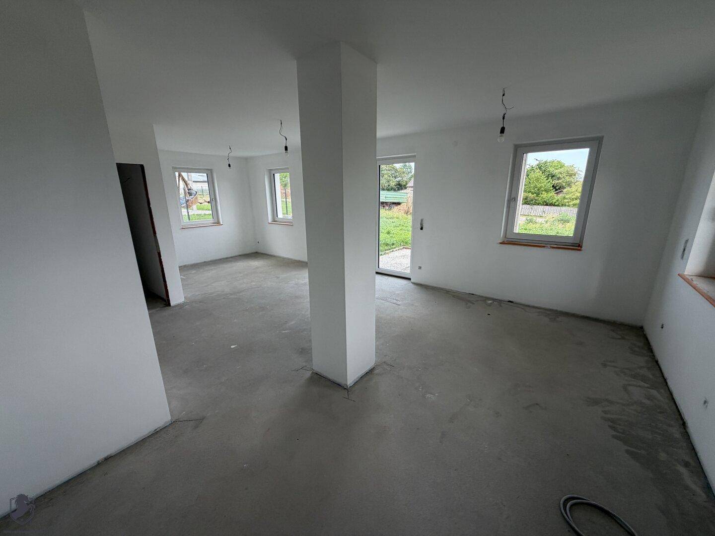 Großzügiger offener Wohn- und Essbereich im Rohbau mit viel Tageslicht und Gartenzugang.