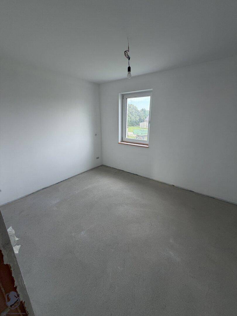 Geräumiges Schlafzimmer im Rohbau mit Fenster und Rohbetonboden, bereit für den Ausbau.