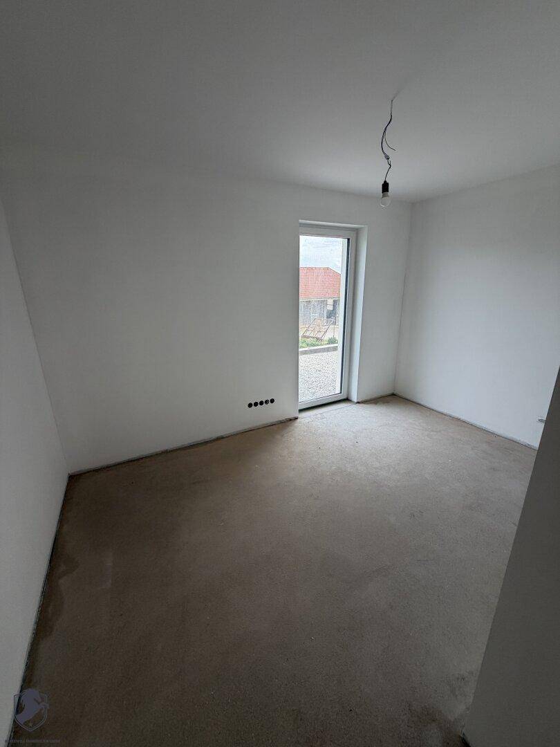 Helles Schlafzimmer im Rohbau mit Zugang zum Außenbereich und Rohbetonboden.