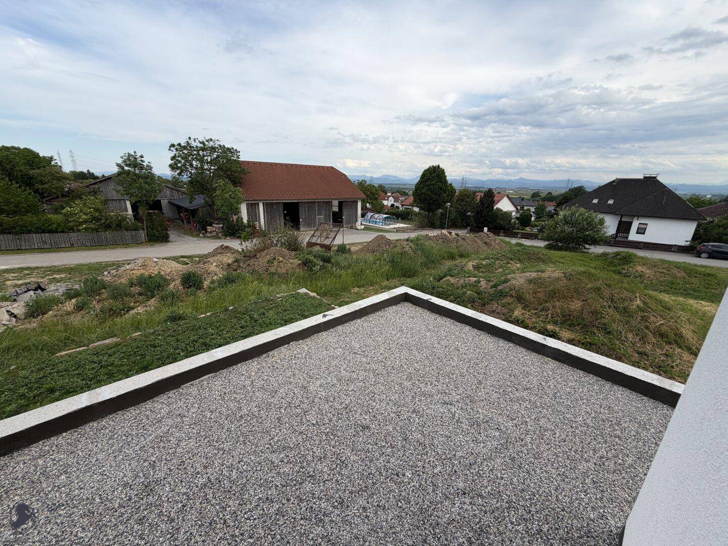Blick von einem Flachdach auf die ländliche Umgebung mit Bergen am Horizont.