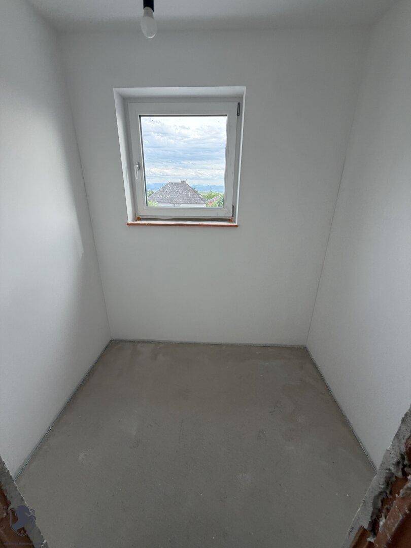 Kleines Zimmer im Rohbau mit Dachschräge und Fenster, ideal als Kinder- oder Gästezimmer.