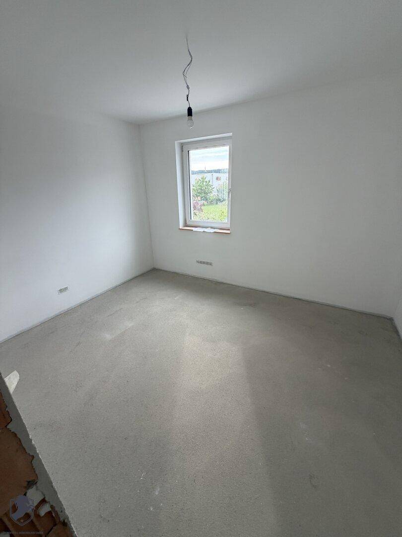 Helles Schlafzimmer im Rohbau mit Fenster und Rohbetonboden, bereit für die Gestaltung.