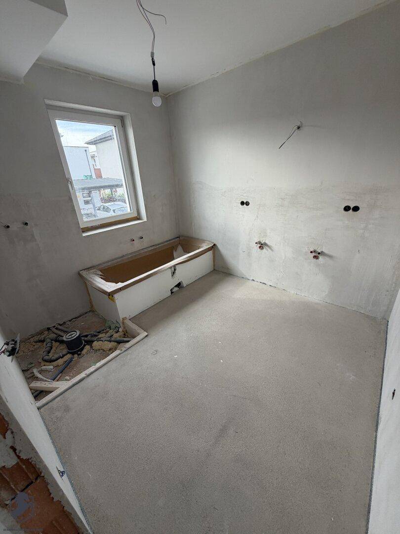Badezimmer im Rohbau mit eingebauter Badewanne und vorbereiteten Anschlüssen.