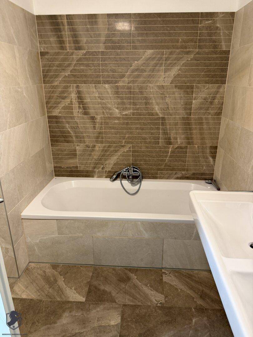 Modernes Badezimmer mit Badewanne und eleganten Fliesen an Wänden und Boden.