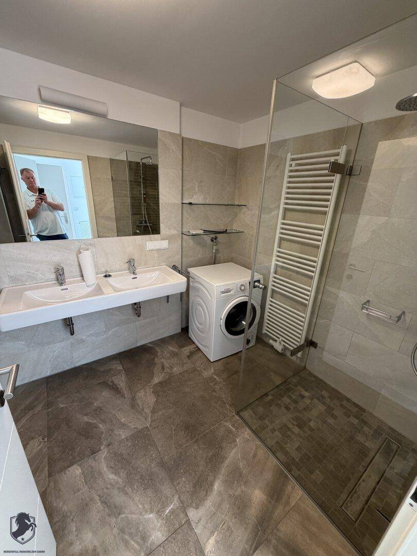 Geräumiges Badezimmer mit Doppelwaschbecken, großer begehbarer Dusche und Waschmaschine.