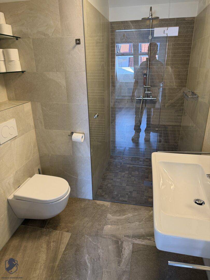 Helles Badezimmer mit wandhängender Toilette, Waschbecken und geräumiger begehbarer Dusche.