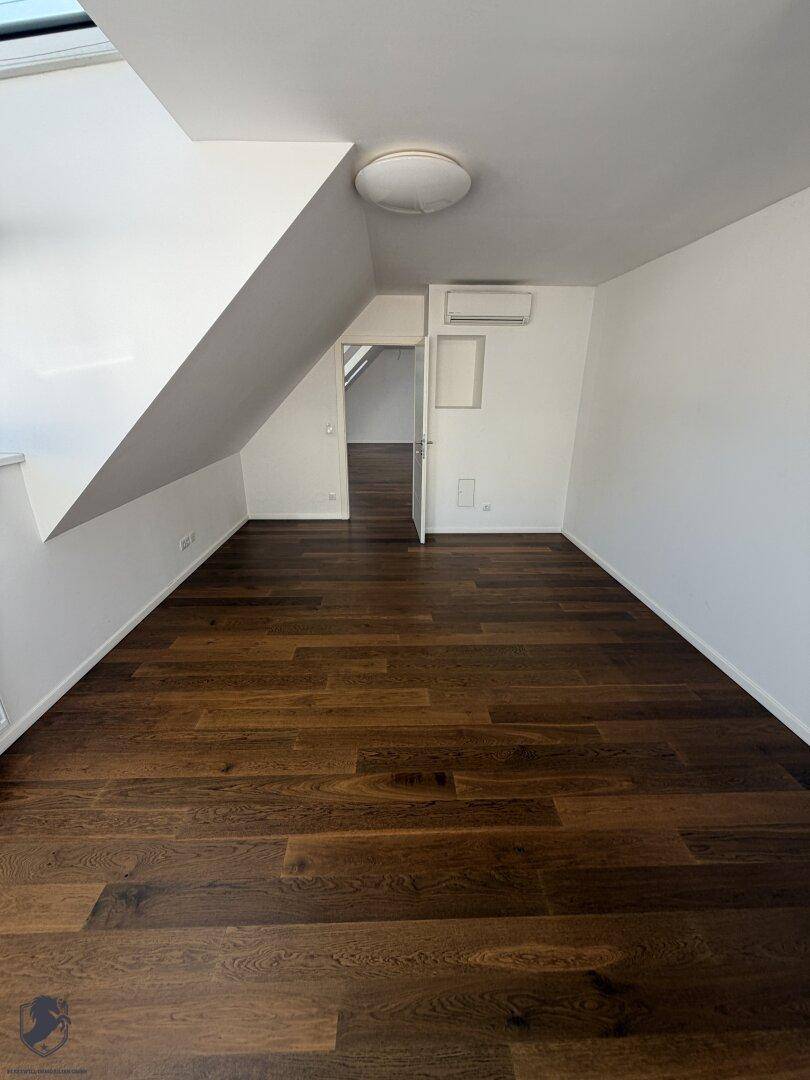 Helles Zimmer im Dachgeschoss mit dunklem Parkettboden und Klimaanlage.