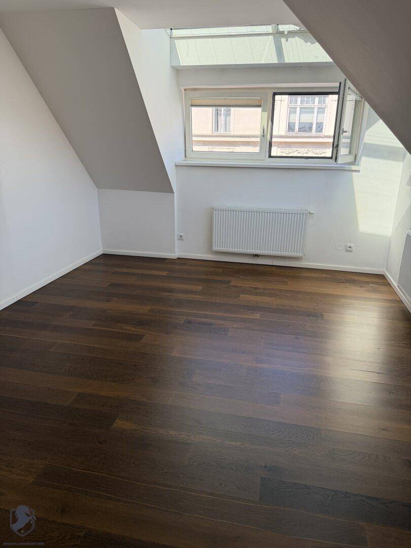 Helles Zimmer im Dachgeschoss mit dunklem Parkettboden und Ausblick.