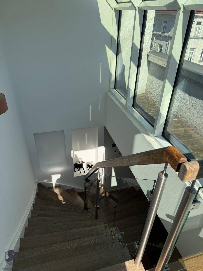 Moderne Treppe mit Glasgeländer und Holzstufen, die zu einem lichtdurchfluteten Bereich führt.