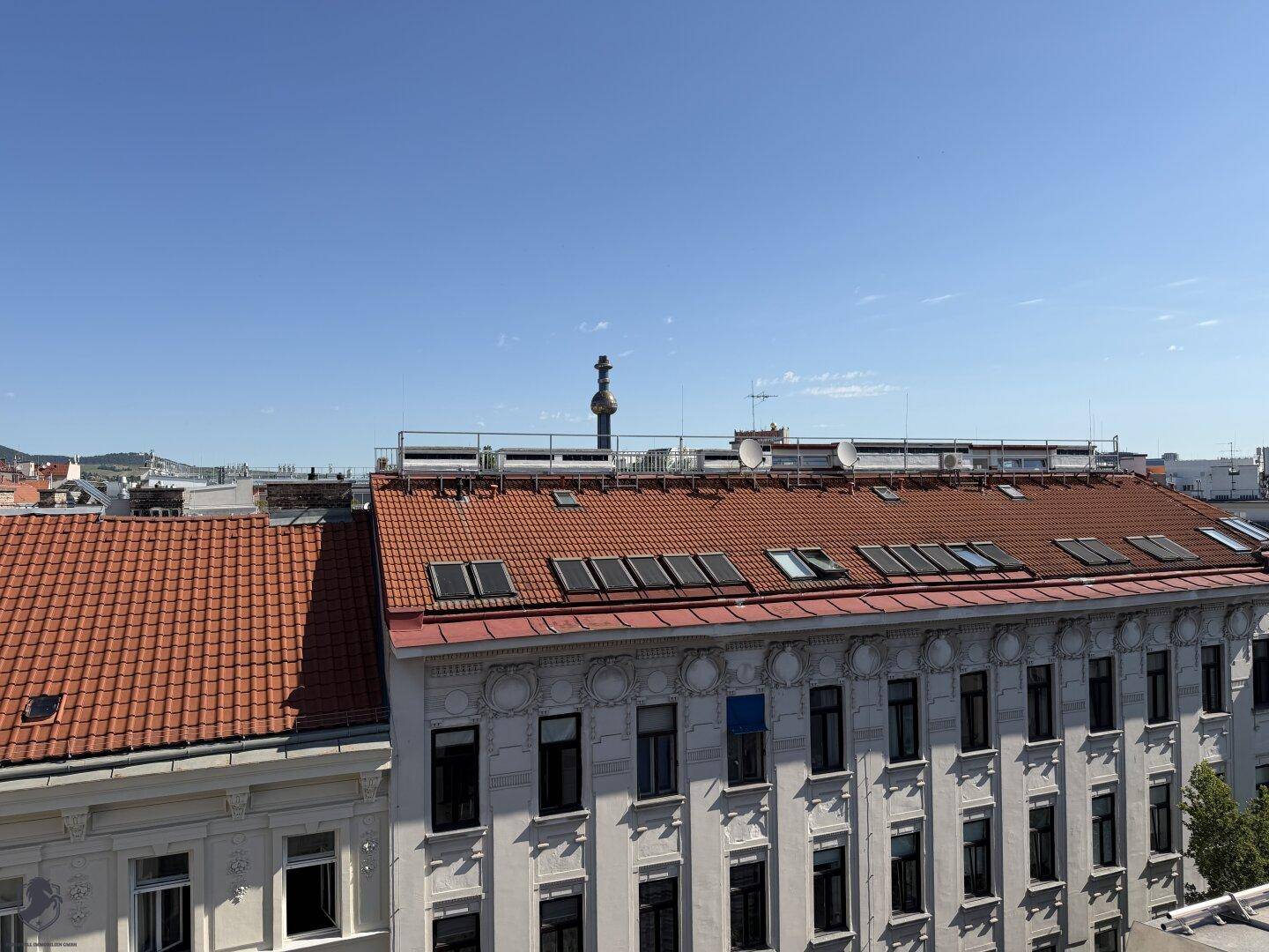 Aussicht über die Dächer der Stadt mit roten Ziegeln und einem markanten Turm am Horizont.