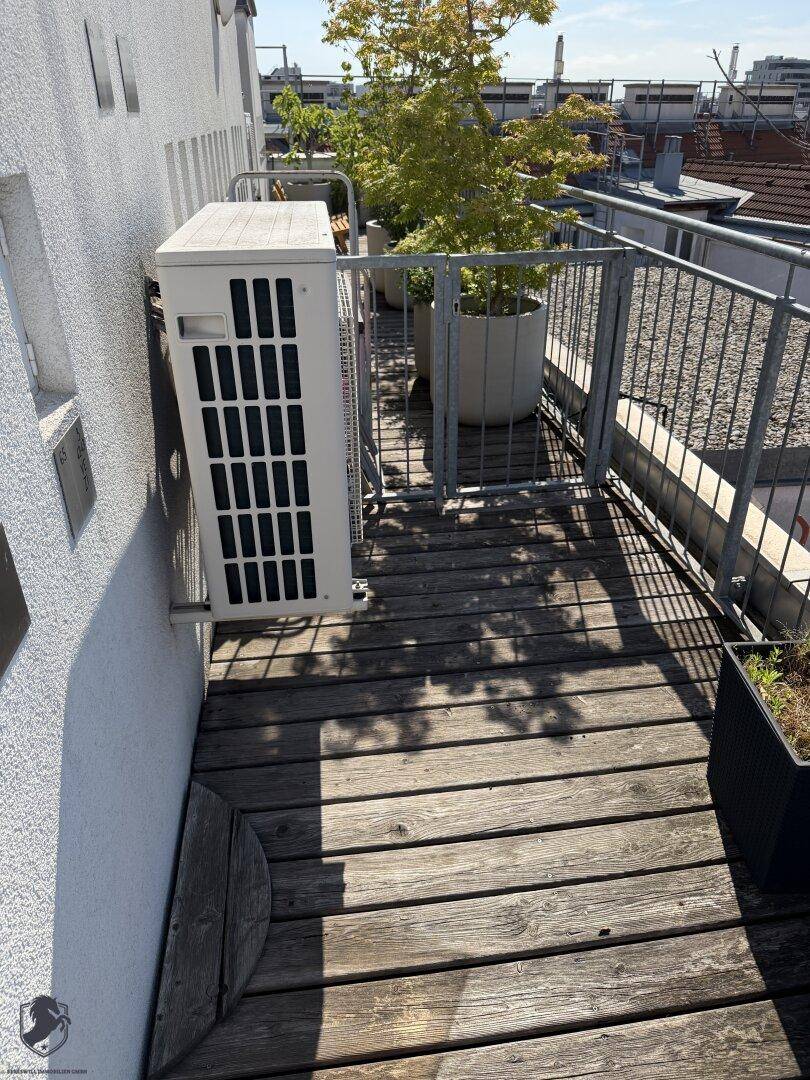 Kleiner Außenbereich mit Holzdeck, Pflanzen und Klimaanlage auf dem Dach.