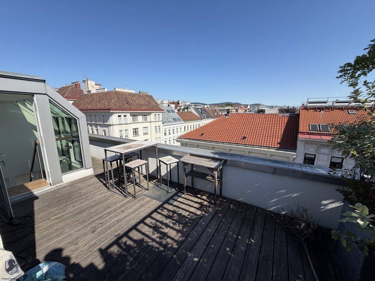 Geräumige Dachterrasse mit Holzdeck, Sitzgelegenheiten und weitem Blick über die Stadt.