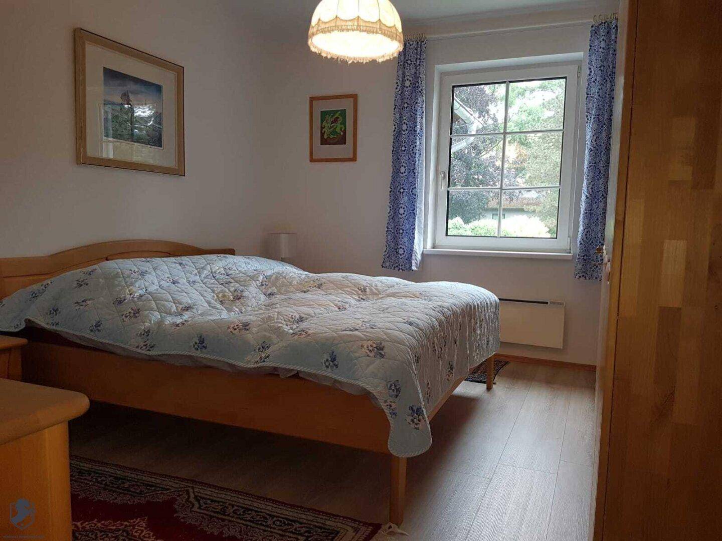 Gemütliches Schlafzimmer mit Holzbett, Kleiderschrank und Fenster mit blauen Vorhängen.