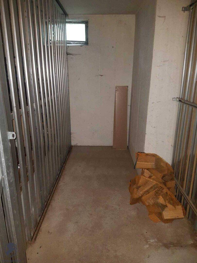 Abstellraum oder Kellerabteil mit Metallabtrennungen, kleinem Fenster und Betonboden.