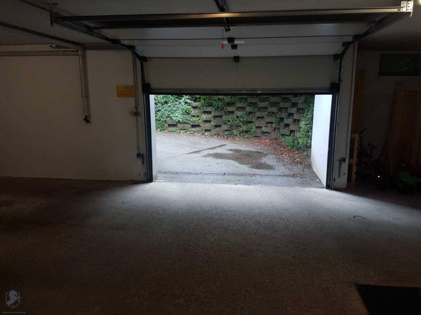 Garageninnenraum mit offenem Tor, das zu einer gepflasterten Einfahrt führt.