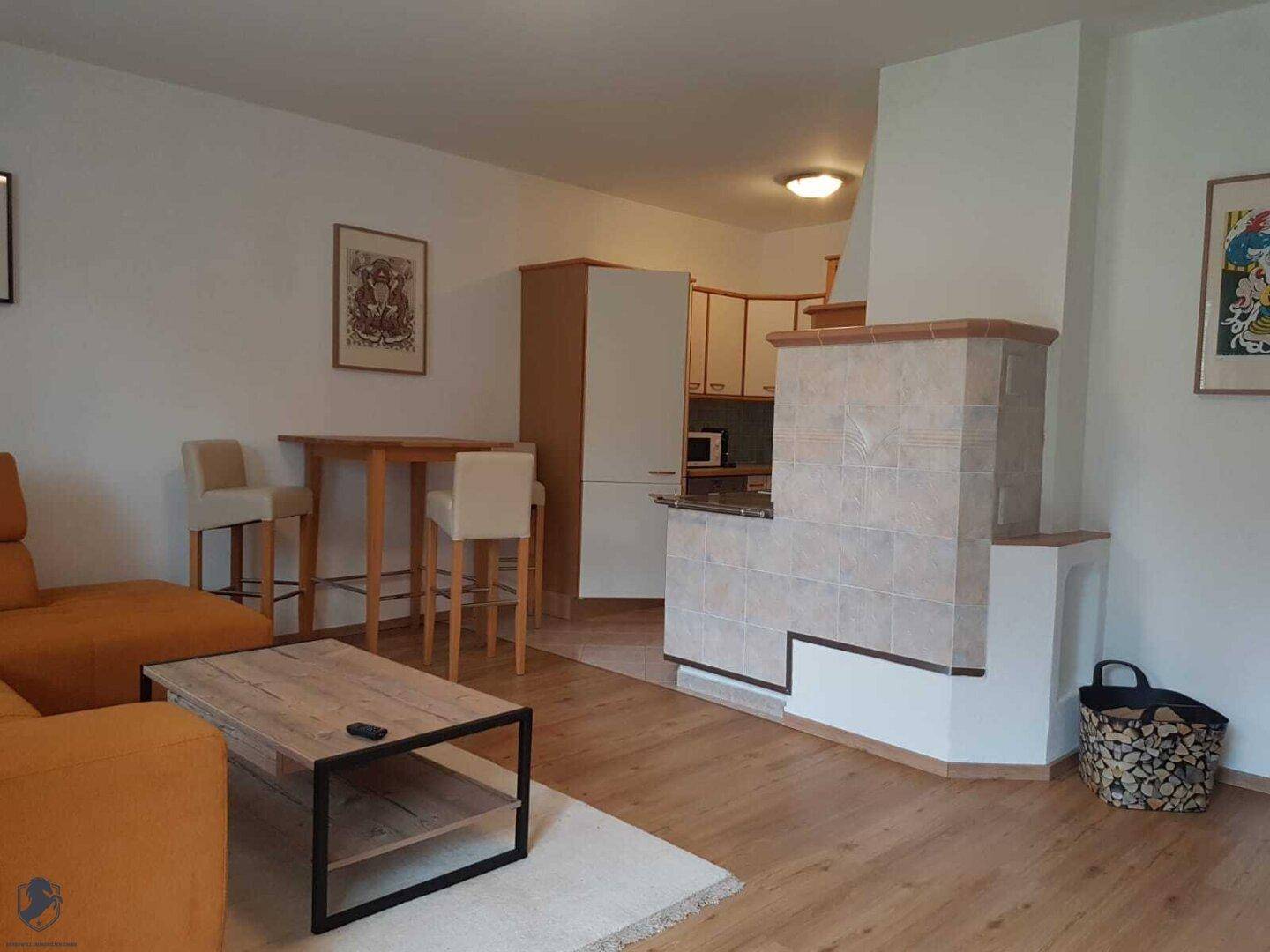 Offener Wohnbereich mit orangefarbenem Sofa, Couchtisch und einem traditionellen Kachelofen.