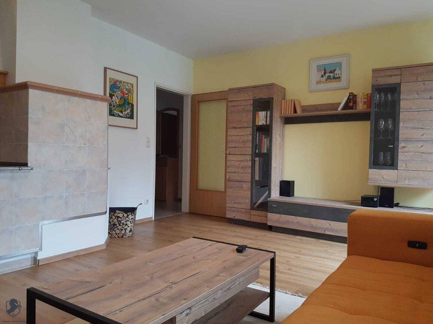 Wohnzimmer mit orangefarbenem Sofa, Holztisch und einem dekorativen Kachelofen.