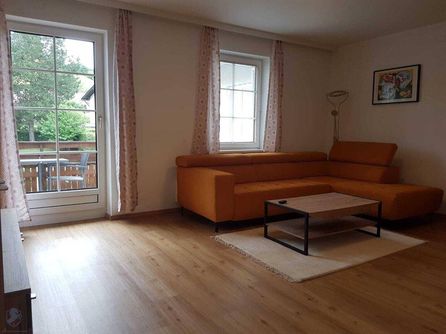 Helles Wohnzimmer mit orangefarbenem Sofa, Holzboden und Zugang zu einem Außenbereich.