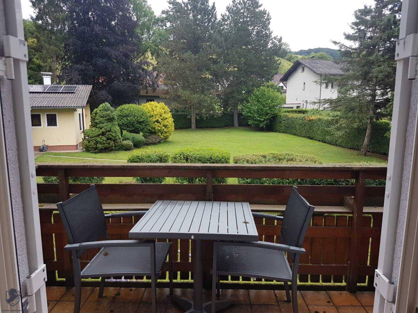Balkon mit kleinem Tisch und Stühlen, bietet einen schönen Blick auf den grünen Garten.