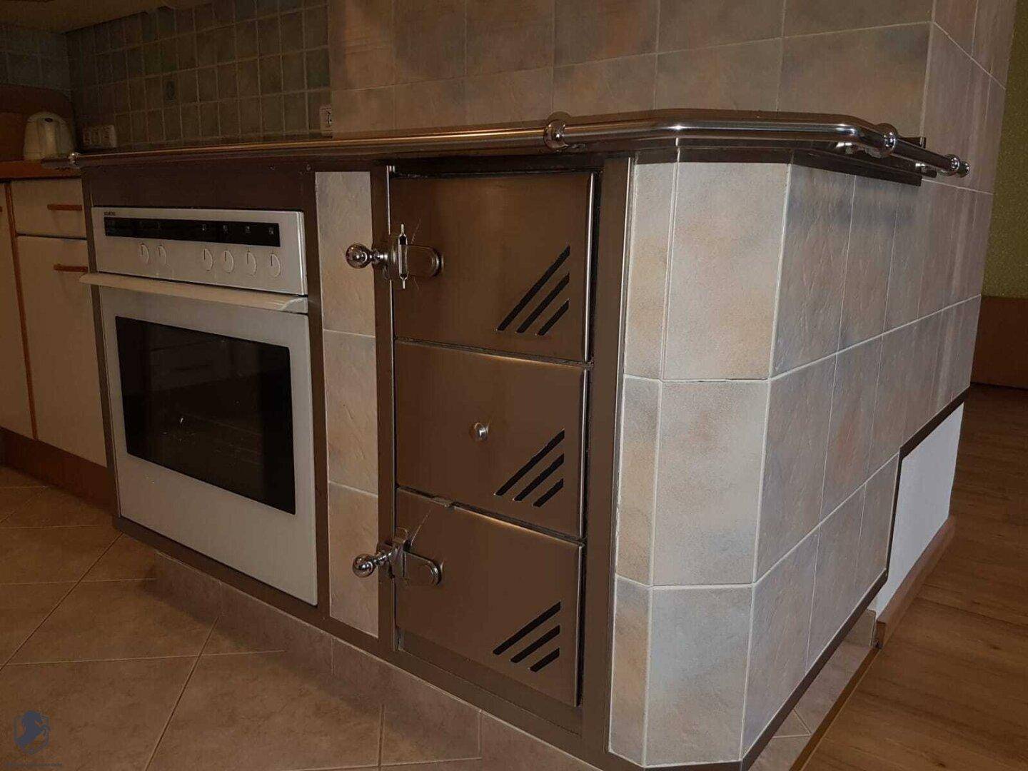 Küche mit traditionellem Kachelofen, integriertem Backofen und Fliesenboden in beigem Farbton.