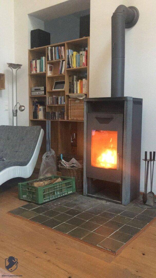 Gemütliches Wohnzimmer mit modernem Holzofen, Bücherregal und Holzboden.