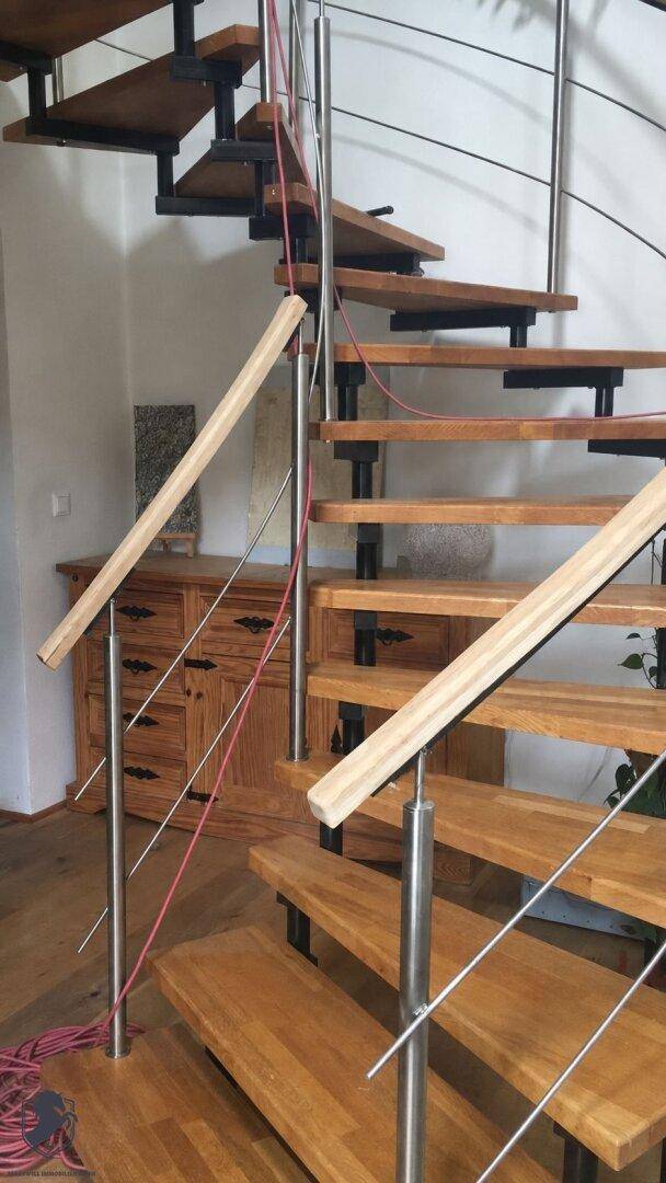 Moderne Holztreppe mit Metallgeländer und offenen Stufen in einem hellen Innenraum.