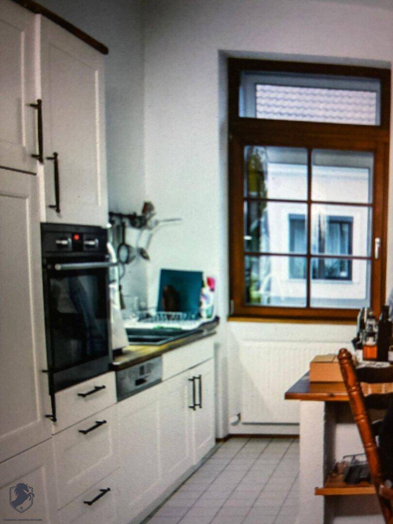 Helle Küche mit weißen Schränken, Einbauofen und einem Fenster mit Blick nach draußen.