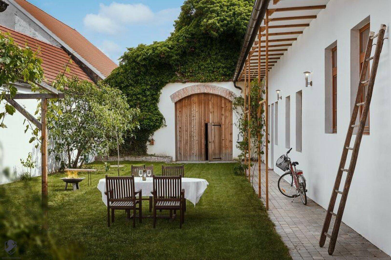 Idyllischer Gartenhof mit Esstisch im Freien, Feuerstelle und einer von Efeu bewachsenen Wand.