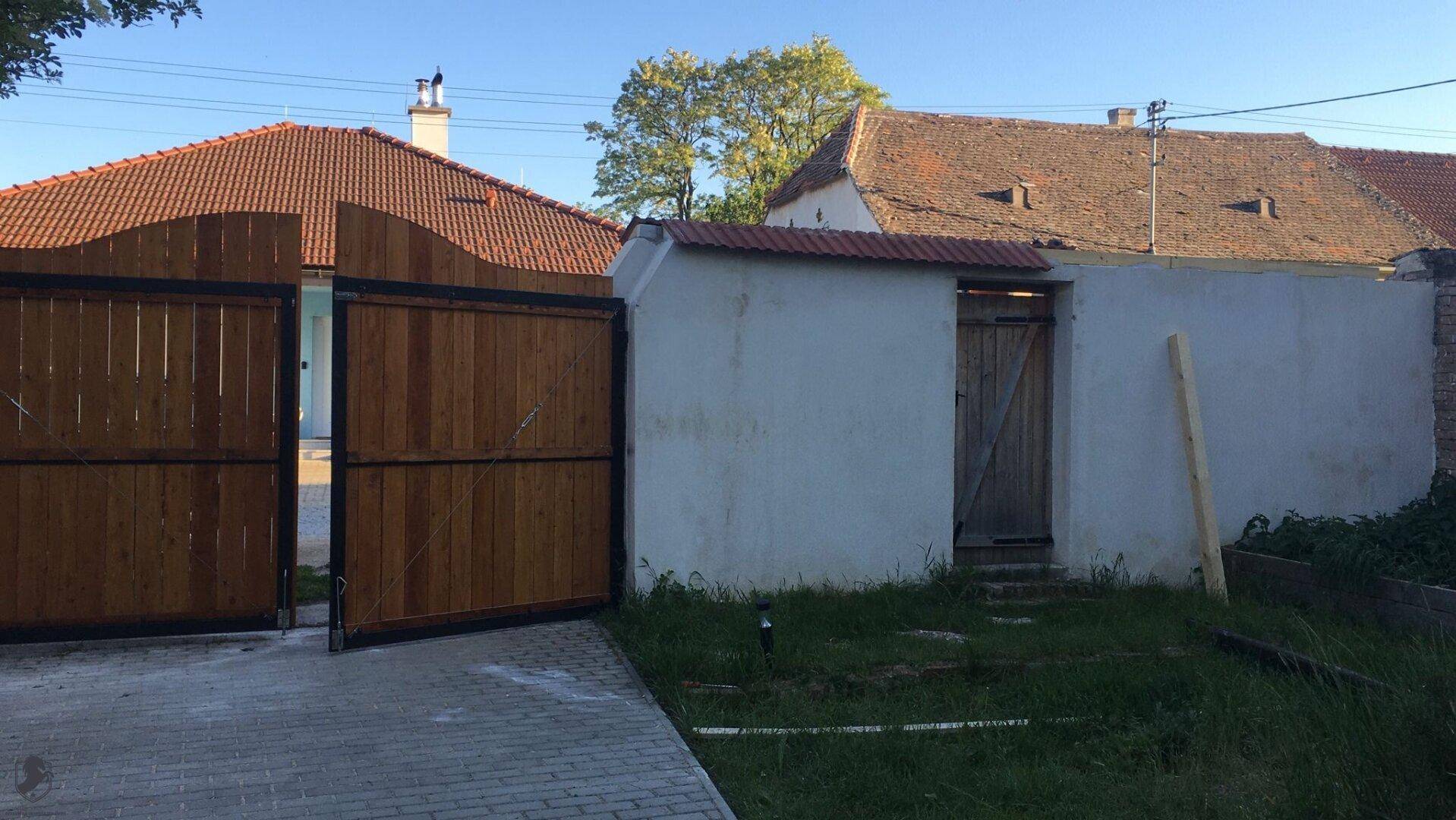 Eingangsbereich eines Anwesens mit großen Holztoren und einem kleinen Nebengebäude.