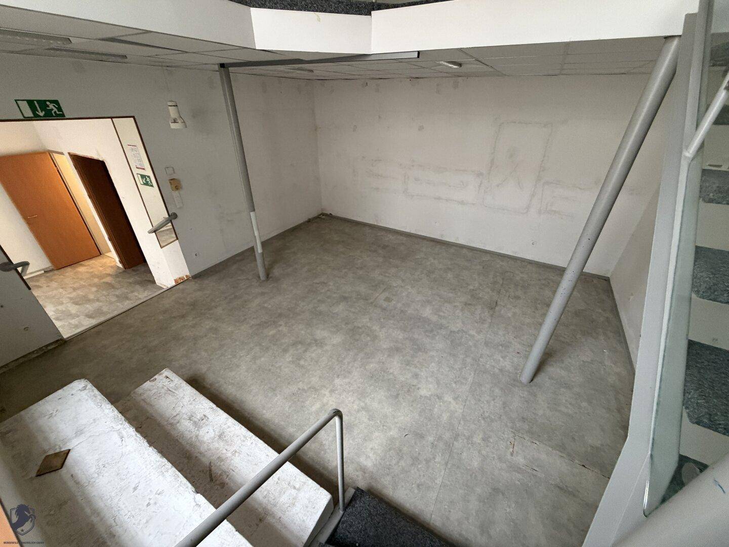 Blick auf die untere Ebene eines Gewerberaums mit Betonboden und Zugang zu weiteren Bereichen.