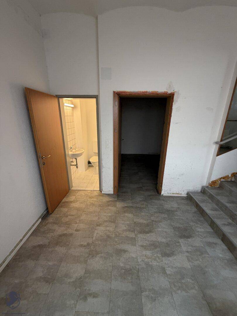 Flur mit hellgrauem Fliesenboden, weißen Wänden und Zugang zu einem Badezimmer und weiteren Räumen.