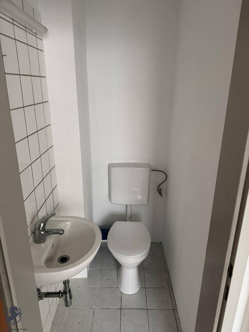 Kleiner Toilettenraum mit weißen Wandfliesen, WC und Waschbecken, funktional und sauber.