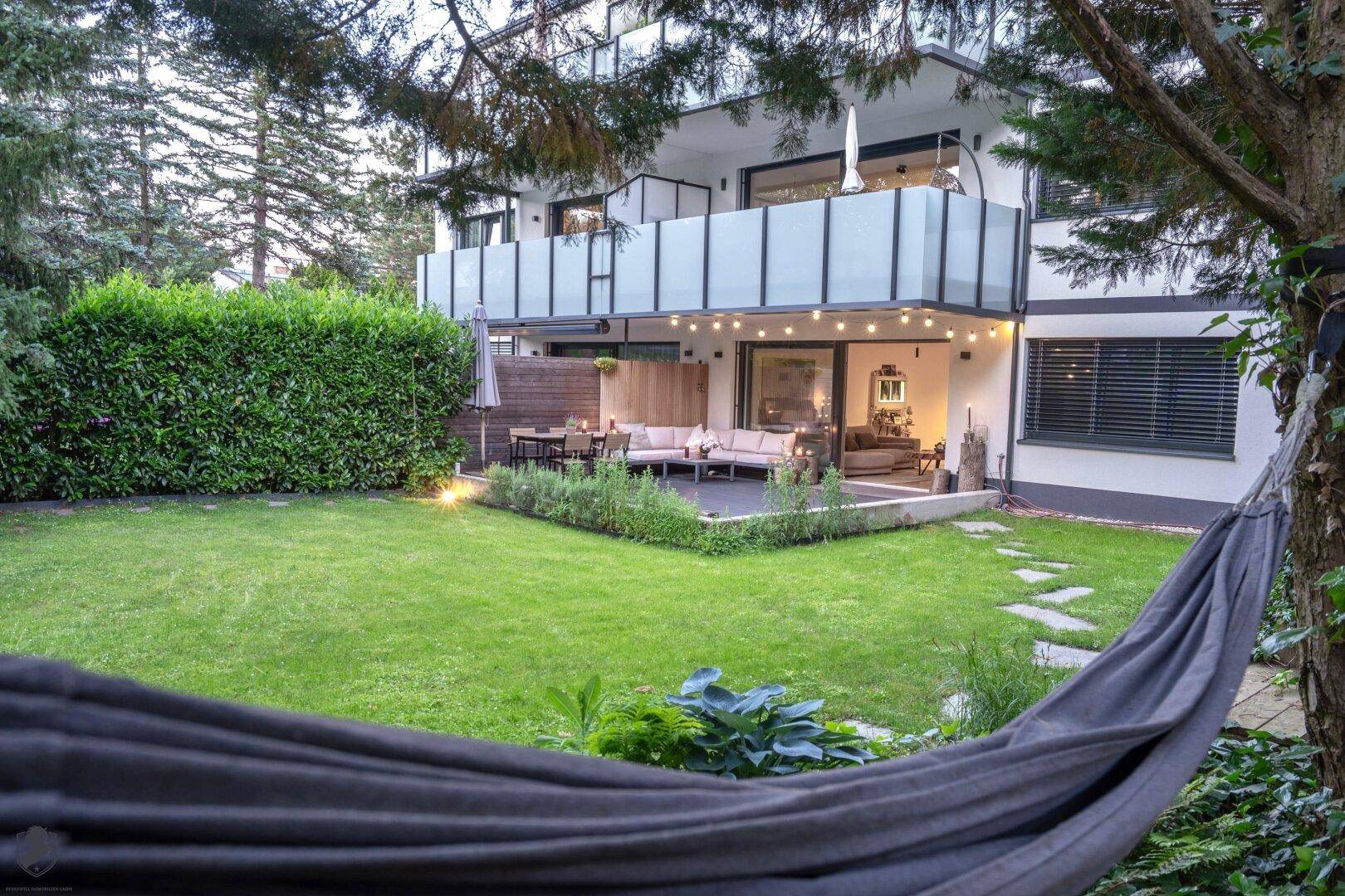 Gepflegter Garten mit Rasenfläche, Hängematte und einer gemütlichen Terrasse im Hintergrund.