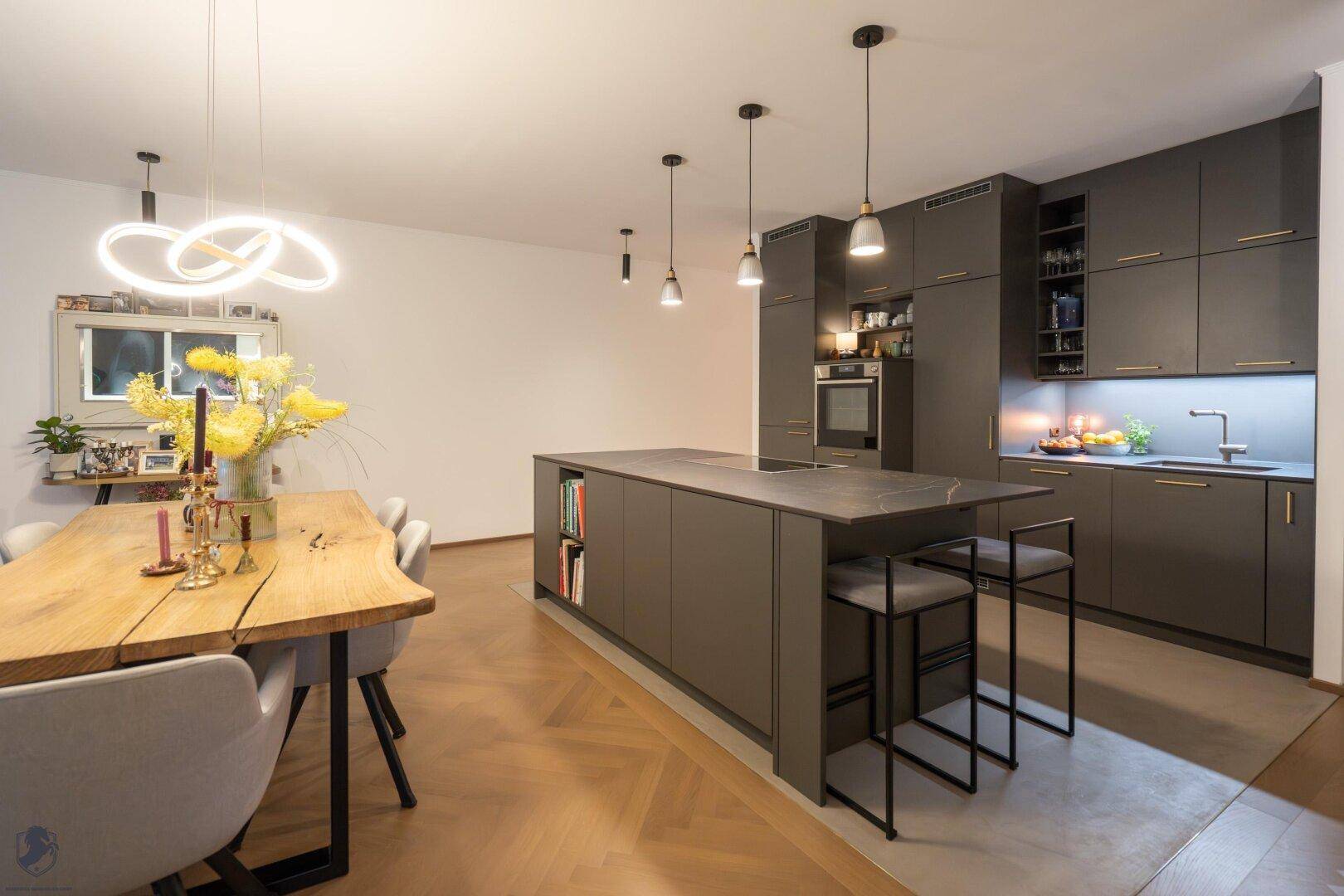 Moderne Küche mit dunklen Schränken, Kücheninsel und integriertem Essbereich.