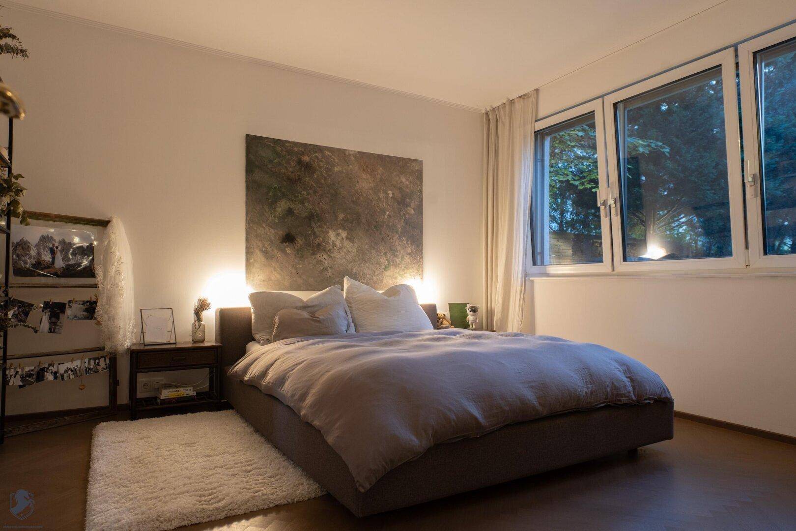 Gemütliches Schlafzimmer mit großem Bett, weichem Teppich und großen Fenstern.